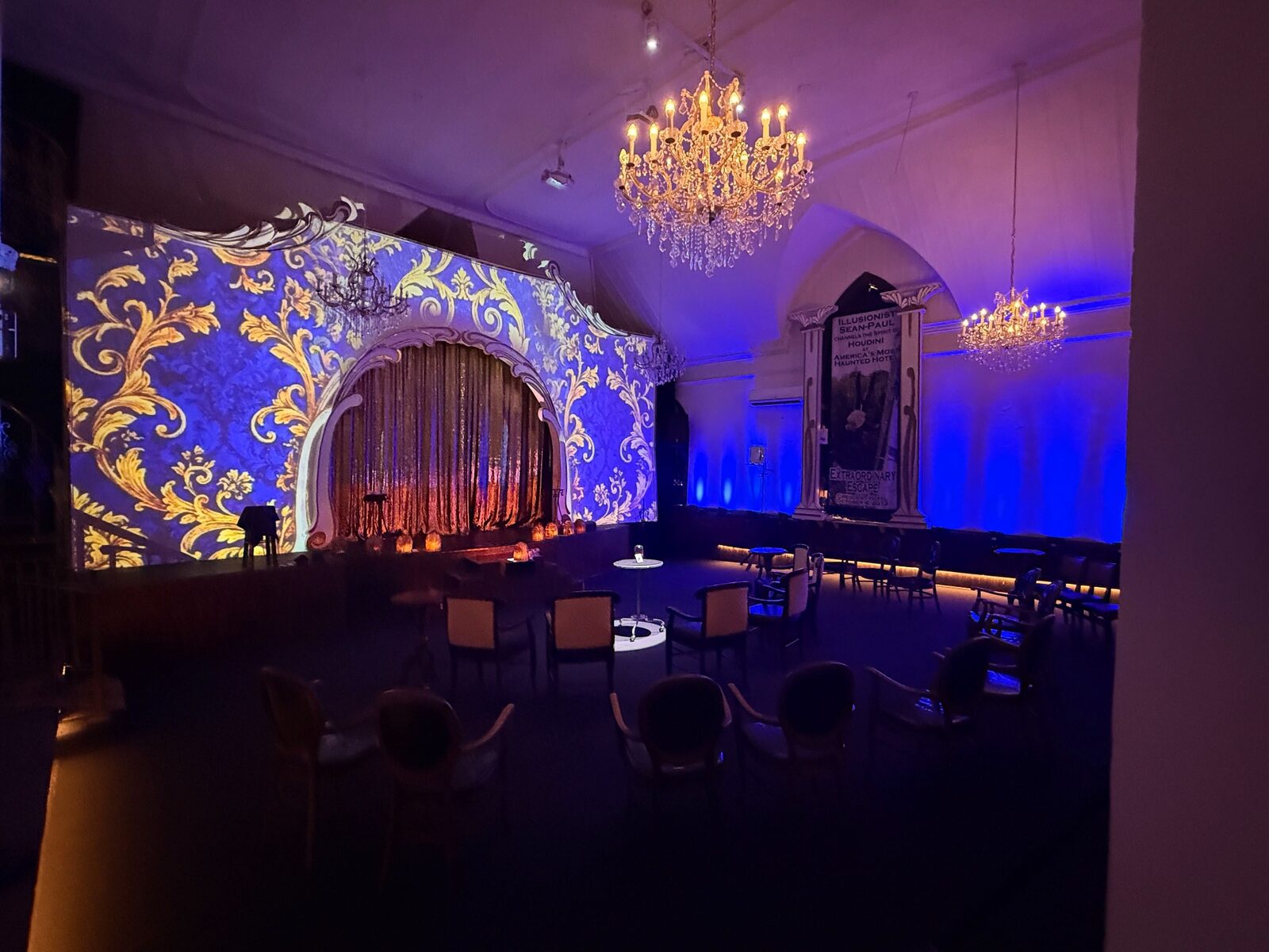 Intrigue Theater interior — chandeliers, intimate seating, and a projection-mapped stage